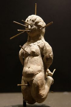 裸体伏都教娃娃跪在姿势上，被13针绑住并刺穿。在一个带有绑定咒语（Katadesmos）的铅片中发现的陶土花瓶中。由Wikimedia Commons提供。