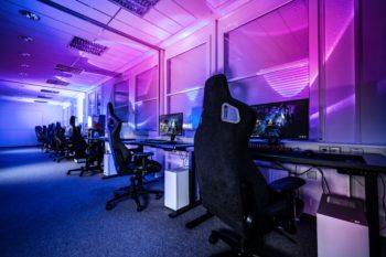 一个摆满电脑和游戏椅的空房间。房间用蓝色和粉色的灯光照明，营造出一种情绪效果。